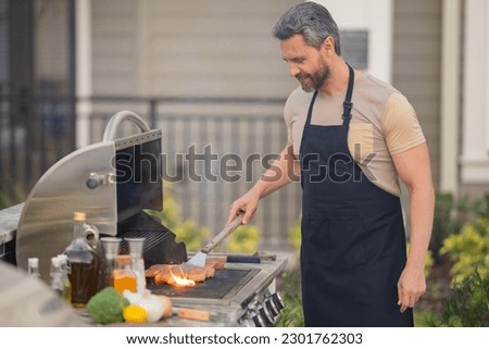 Grill and barbecue cook. Chef with BBQ cooking tools. Barbecue and grill. Picnic barbecue party. Chief cook with utensils for barbecue grill. Barbeque on holiday picnic. Man grilling a steak on BBQ.