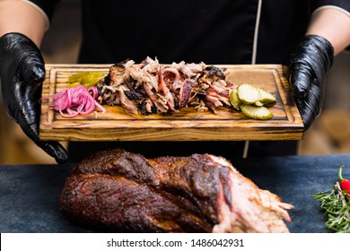 Grill restaurant kitchen. Chef hands in black cooking gloves holding smoked pulled pork with pickles on wooden board. - Powered by Shutterstock