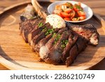 Grill tomahawk on wooden late with tomato salad. Selective focus, close up food.Great concept for beach club menu. Earthy background tone 