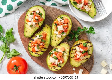 Grilled Avocado Stuffed With Tomatoes, Goat Cheese, Parsley, And Olive Oil On A Cutting Board. Top View, Grey Background