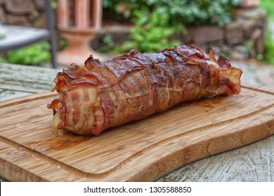 Grilled Bacon-wrapped Pork Tenderloin On A Wooden Plate On A Wooden Table Outside