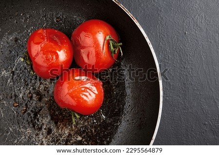 Grilled baked tomatoes in a black frying pan on a black concrete background. Top view with copy space