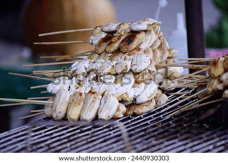 Grilled banana in bamboo skewers on gridiron for selective focus to sold at the local market in Thailand.