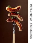 Grilled Bavarian sausages with rosemary.  Sausages  on a fork sprinkled with rosemary. Brown background.