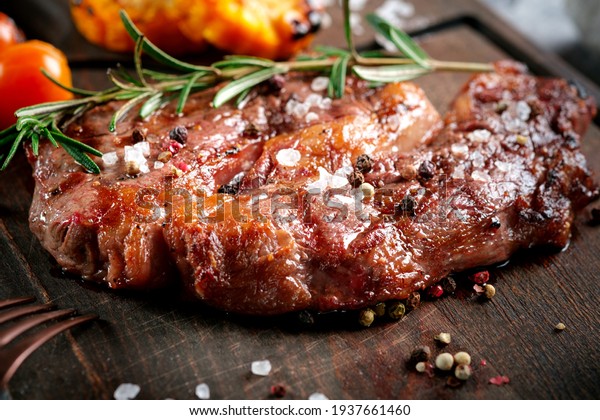 Grilled beef Rib Eye steak served on a wooden board\
with tomatoes and rosemary. Recipe for cooking steak with\
vegetables. Close up