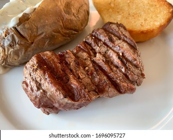 Grilled Beef Steak Filet Mignon On The Plate High Angle View With Garlic Baguette, Baked Potato With Sour Cream On The White Plate. Dinner In The Steak House