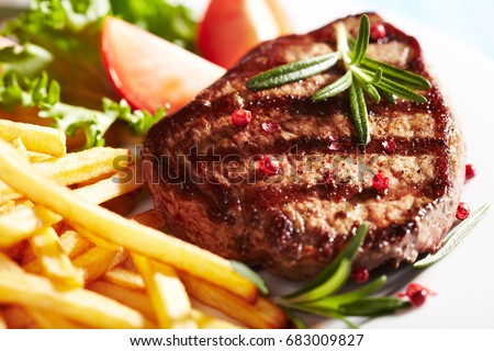Grilled beef steak with french fries, tomatoes, lettuce and fresh rosemary. Home made food. Concept for a tasty and heart meal. Close up. 