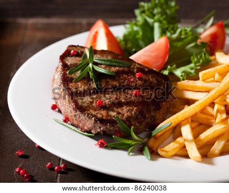 Grilled beef steak with french fries, tomatoes, lettuce and fresh rosemary. Home made food. Concept for a tasty and hearty meal.  Rustic wooden background. Close up.