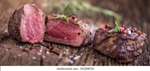 Grilled beef steak with rosemary, salt and pepper on old wooden board.