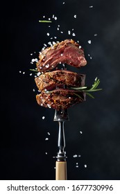 Grilled beef steak with spices on a black background. Beef steak on a fork sprinkled with rosemary and sea salt.   