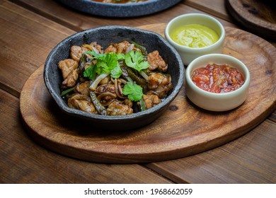 Grilled beef sweetbreads on a wooden plate accompanied by sauce on a wooden table