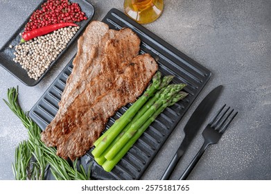 Grilled beef, thin slices of beef bacon on a cutting board with asparagus garnish. Top view. Copy space