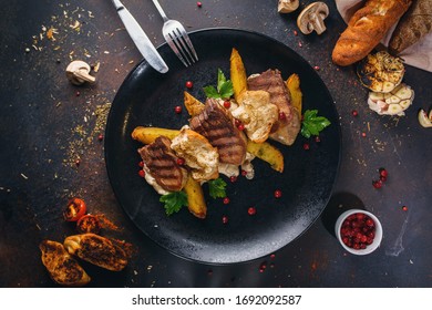 Grilled beef tongue with fried potato and singed bread hot dish on a plate among green and ingredients on rusty craft background