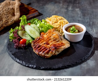 Grilled Boneless Chicken Steak with chili sauce, salad, noodles in a dish side view on dark background