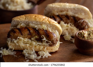 Grilled bratwurst with sauerkraut on a bun and mustard in a bowl on a wooden board
