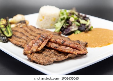 Grilled Carne Asada Steak Topped With Chorizo Served On A Plate With Rice And Beans.