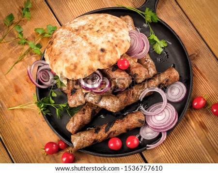 Grilled cevapi with bread, onion, cherry tomatoes and parsley on wooden table, top view