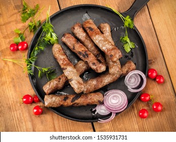 Grilled cevapi in a cast iron pan on wood, top view