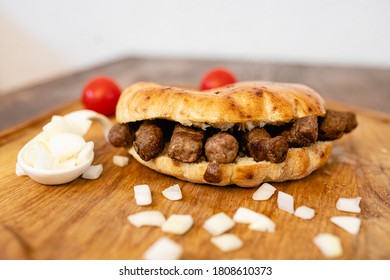 Grilled cevapi / cevapcici with bread, onion, cherry tomatoes on wooden table