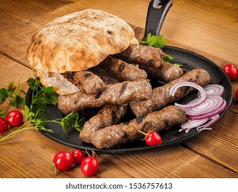 Grilled cevapi with roasted bread bun in a pan on wood