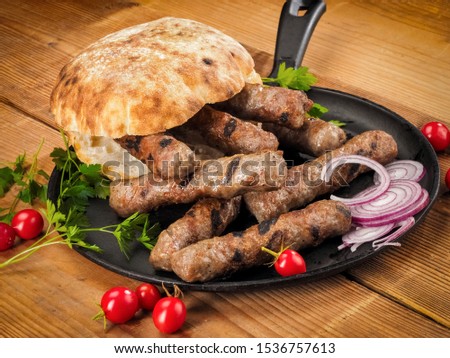 Grilled cevapi with roasted bread bun in a pan on wood