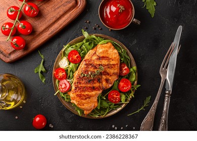 Grilled chicken breast with arugula and tomatoes on a plate, top view, black food background. High quality photo - Powered by Shutterstock