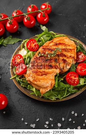 Grilled chicken breast with arugula and tomatoes on a plate and black table vertical photo. High quality photo