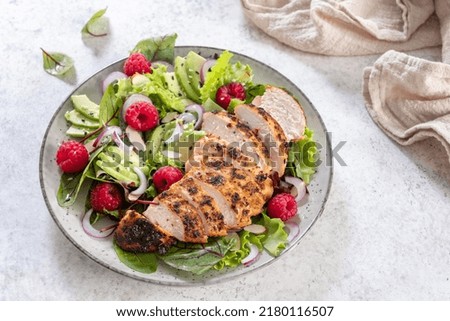 Grilled chicken breast, fillet and fresh vegetable salad of lettuce, arugula, spinach, avocado, onion and pecan nut with raspberry. Summer salad, healthy eating. Fresh healthy food.