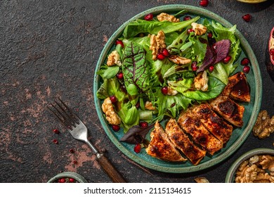 Grilled chicken breast fillet and mix salad with walnuts, pomegranate and balsamic sauce on dark background with fork. top view. healthy food