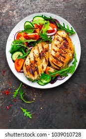 Grilled chicken breast. Fried chicken fillet and fresh vegetable salad of tomatoes, cucumbers and arugula leaves. Chicken meat with salad. Healthy food. Flat lay. Top view. Dark background