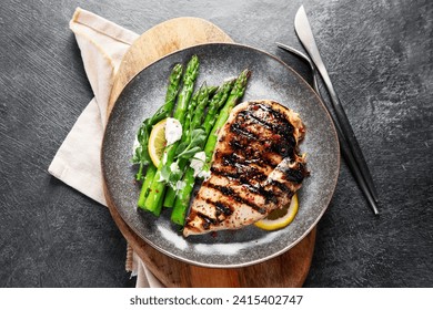 Grilled chicken breast and garnish of asparagus on a dark background. Top view. - Powered by Shutterstock