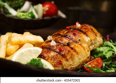 grilled chicken breast with green salad and french fries on a black plate. - Shutterstock ID 435472501
