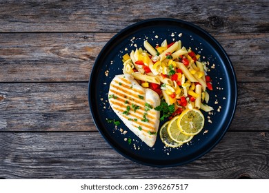 Grilled chicken breast with penne noodles, lemon and pepper on wooden background  - Shutterstock ID 2396267517