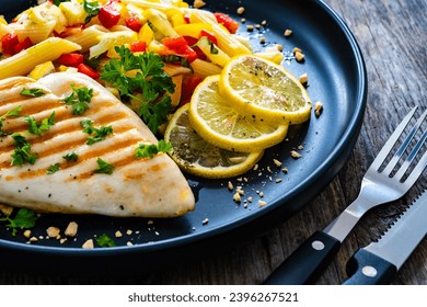 Grilled chicken breast with penne noodles, lemon and pepper on wooden background  - Shutterstock ID 2396267521