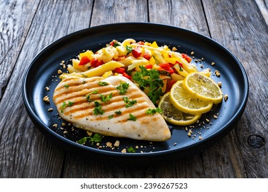 Grilled chicken breast with penne noodles, lemon and pepper on wooden background  - Shutterstock ID 2396267523