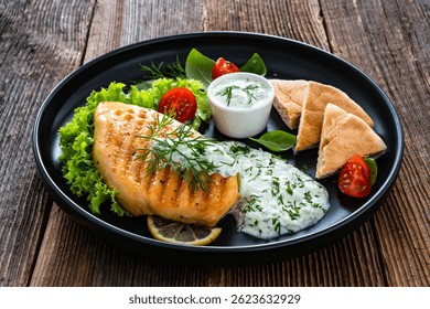 Pechuga de pollo a la parrilla, pan pita y salsa tzatziki en la mesa de madera. Comida de estilo griego