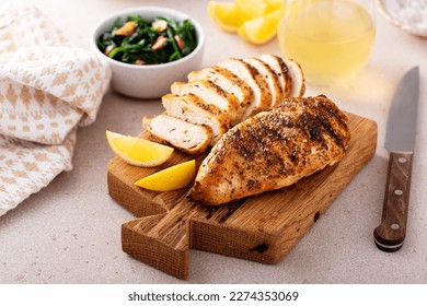Grilled chicken breast with spice rub and lemon on a cutting board, sliced and whole - Shutterstock ID 2274353069