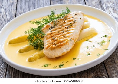 Grilled chicken breast and white asparagus in hollandaise sauce on wooden table 