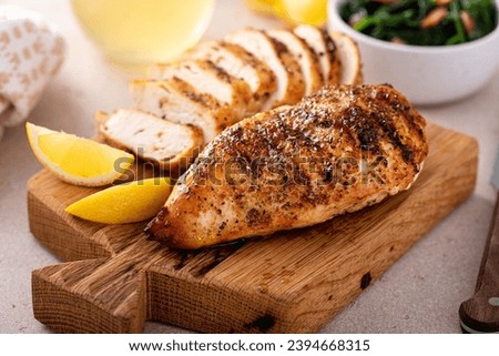 Grilled chicken breast whole and sliced on a cutting board with fresh lemon