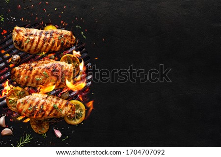 Grilled chicken breasts on a grill plate on black background with copy space, top view. Bbq background