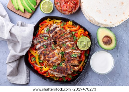 Grilled chicken Fajitas with bell pepper and onion in a pan, served with salsa Asada, sour cream, avocado and tortillas, Southwest Tex-Mex Cuisine, horizontal, top view