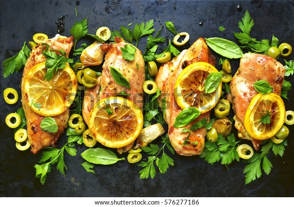 Grilled chicken fillet\
with lemon,green olives and herbs on a black metal tray.Top view\
with space for text.