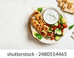 Grilled chicken kebab with fresh vegetable salad on white background, top view, copy space. Mediterranean lunch with roasted skewers, tzadziki sauce and veggies, healthy food.