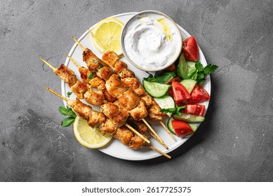 Grilled chicken kebabs with fresh vegetable salad and labneh dip on concrete table, top view. Mediterranean keto lunch with roasted meat souvlaki skewers, tzatziki sauce, healthy greek food.