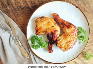 Grilled Chicken Leg Quarters With Crispy Golden Brown Skin, Parsley On White Plate On Dark Wooden Boards. Food Background. Top View .