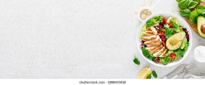 Grilled chicken meat and fresh vegetable salad of tomato, avocado, lettuce and spinach. Healthy and detox food concept. Ketogenic diet. Buddha bowl dish on white background, top view. Banner.