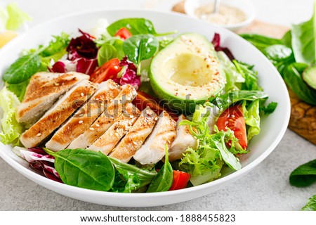 Grilled chicken meat and fresh vegetable salad of tomato, avocado, lettuce and spinach. Healthy and detox food concept. Ketogenic diet. Buddha bowl dish on white background