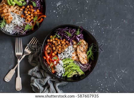 Grilled chicken, rice, spicy chickpeas, avocado, cabbage, pepper buddha bowl on dark background, top view. Delicious balanced food concept    