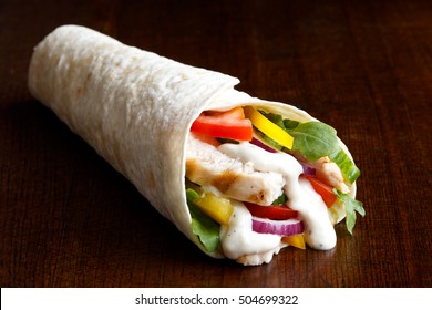 Grilled Chicken And Salad Tortilla Wrap With White Sauce Isolated On Dark Background.