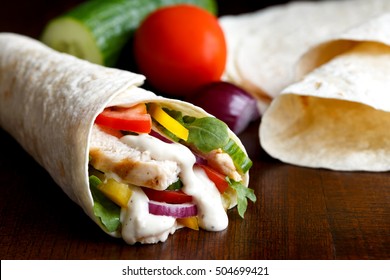 Grilled Chicken And Salad Tortilla Wrap With White Sauce Isolated On Dark Background. Next To Plain Tortillas And Vegetables.